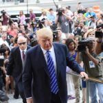 Donald Trump walks up steps through a crowd as A. J. Calloway films nearby