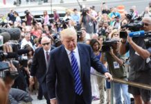 Donald Trump walks up steps through a crowd as A. J. Calloway films nearby