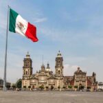 Mexican flag flying over a historic cathedral in a large plaza