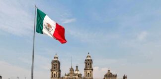 Mexican flag flying over a historic cathedral in a large plaza