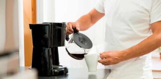 Person pouring coffee from carafe into mug beside drip coffee maker