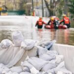 Monsoon Chaos—Workers Vanish In Tunnels Sandbags stacked near a flooded street with rescue workers in a boat