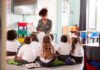 Teacher reading a book to a group of young students on the classroom floor