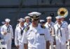 naval officer in white uniform stands before a military band