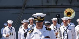 naval officer in white uniform stands before a military band