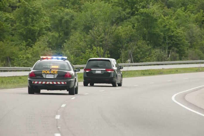 Police car with flashing lights following a minivan on a highway