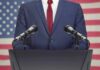 Speaker in suit at podium with microphones