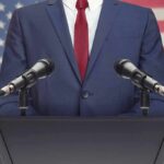 Speaker in suit at podium with microphones