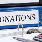 Blue binder labeled donations on a desk with papers and a calculator