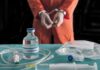 Witnesses Heard Her Breathing After Two Doses Handcuffed person in orange jumpsuit behind medical vials and IV equipment